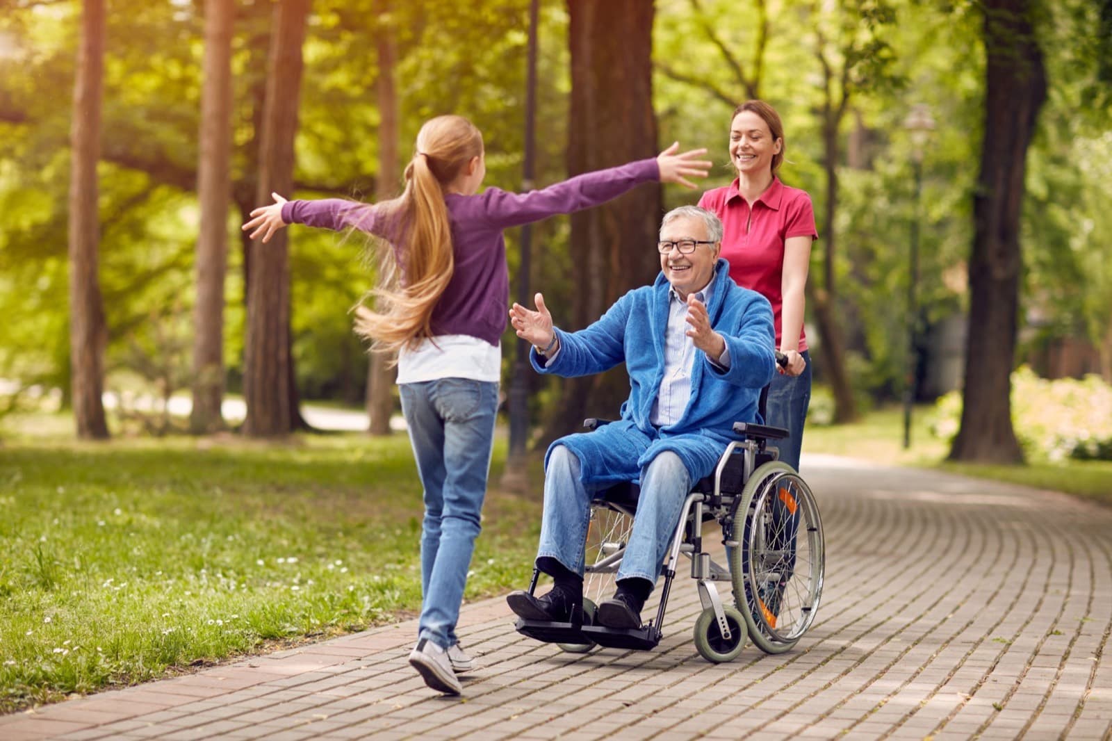 An older man in a wheelchair greeting his granddaughter outdoors